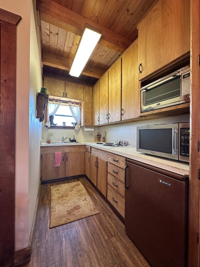 kitchen with light countertops, stainless steel microwave, dark wood finished floors, wood ceiling, and beam ceiling