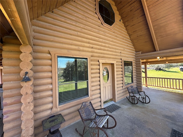 view of exterior entry with log siding, visible vents, and a porch