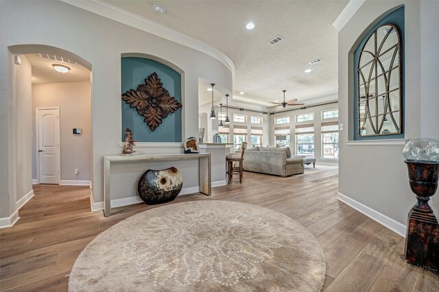 entryway with visible vents, baseboards, ornamental molding, wood finished floors, and ceiling fan