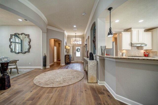 foyer with baseboards, arched walkways, ornamental molding, and wood-type flooring