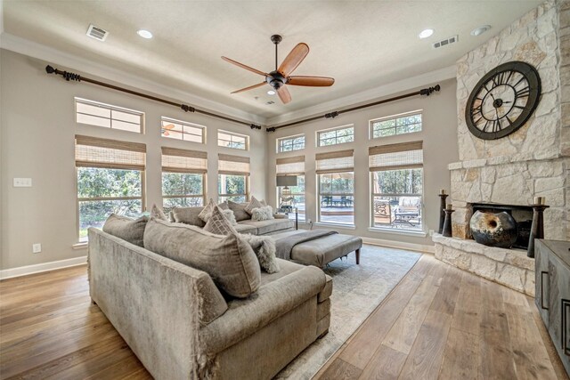 living room featuring light wood-style flooring, ceiling fan, visible vents, and a stone fireplace