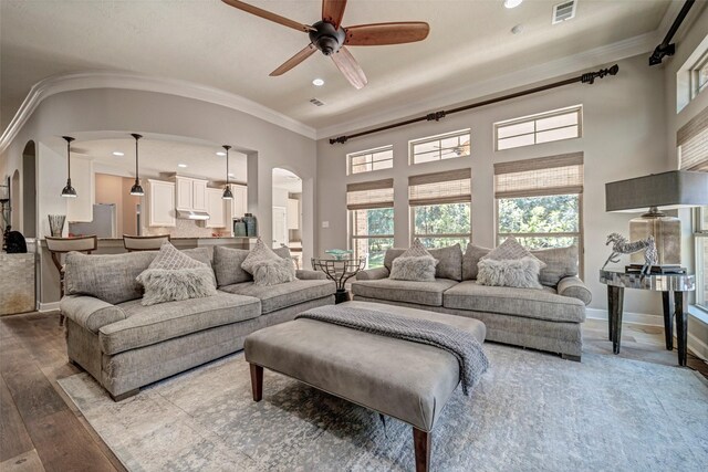 living room with crown molding, hardwood / wood-style floors, arched walkways, visible vents, and a ceiling fan