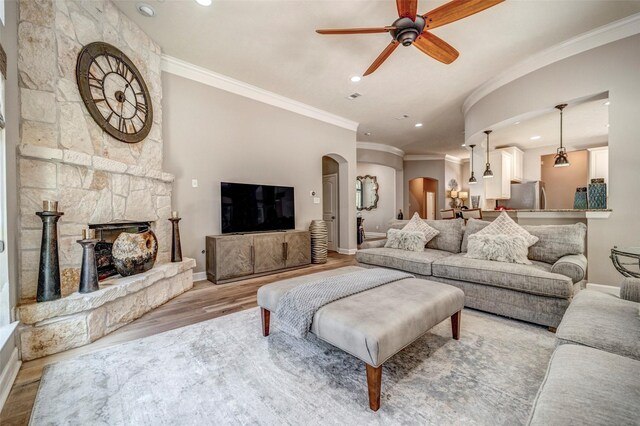 living area featuring a ceiling fan, arched walkways, crown molding, and wood finished floors