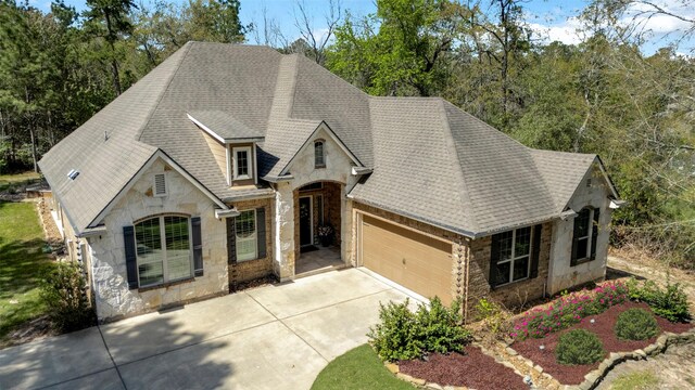french country inspired facade featuring an attached garage, stone siding, and roof with shingles