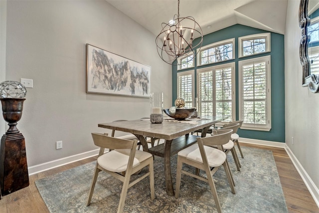 dining room featuring a notable chandelier, baseboards, vaulted ceiling, and wood finished floors