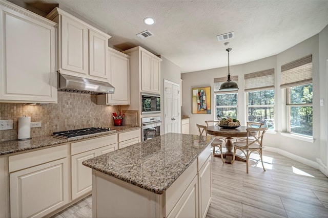 kitchen featuring visible vents, light stone countertops, appliances with stainless steel finishes, under cabinet range hood, and backsplash