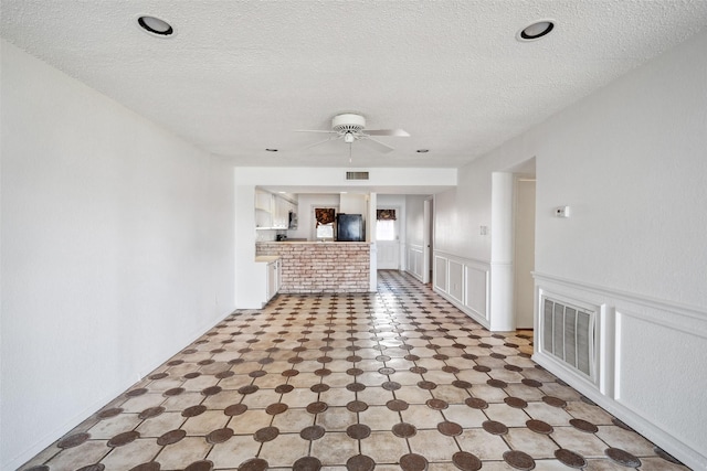 unfurnished living room with a ceiling fan, a textured ceiling, and wainscoting