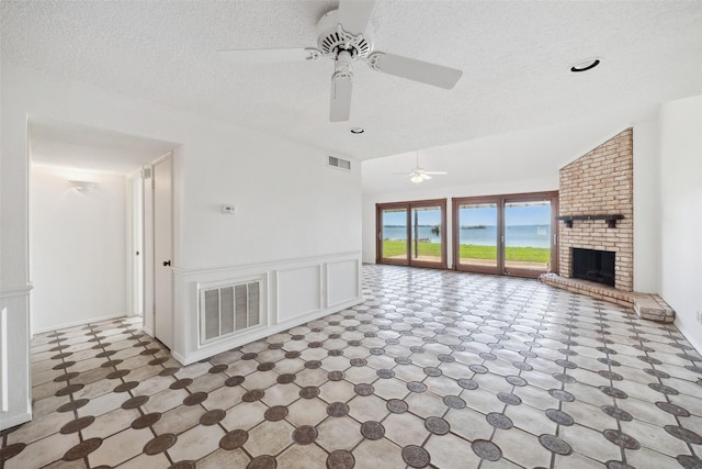 unfurnished living room featuring ceiling fan, a textured ceiling, tile patterned floors, and a brick fireplace