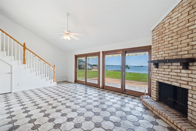 unfurnished living room with lofted ceiling, a water view, a ceiling fan, healthy amount of natural light, and stairway