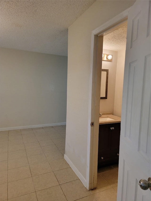 hall featuring baseboards, a textured ceiling, a sink, and light tile patterned floors