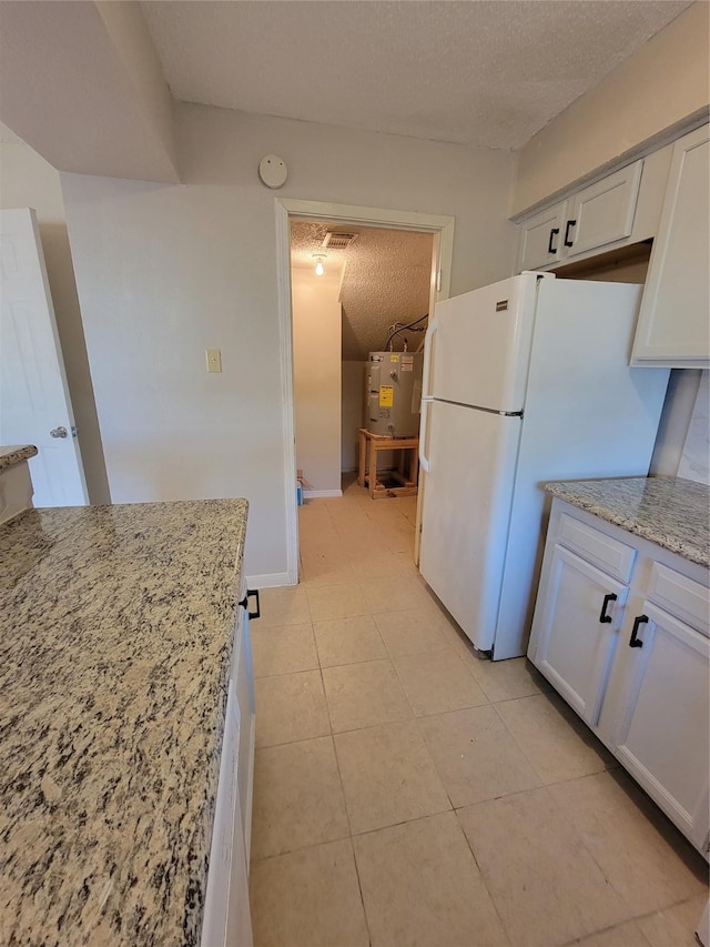 kitchen featuring water heater, light tile patterned floors, a textured ceiling, freestanding refrigerator, and light stone countertops