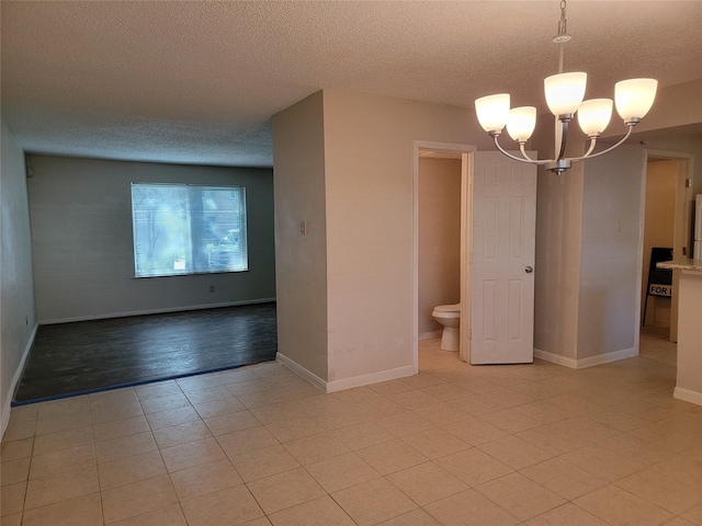 unfurnished room featuring baseboards, a textured ceiling, an inviting chandelier, and light tile patterned flooring