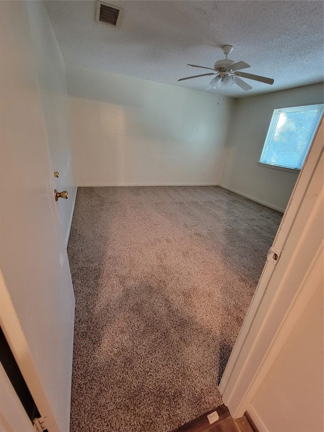 spare room featuring visible vents, ceiling fan, carpet, and a textured ceiling