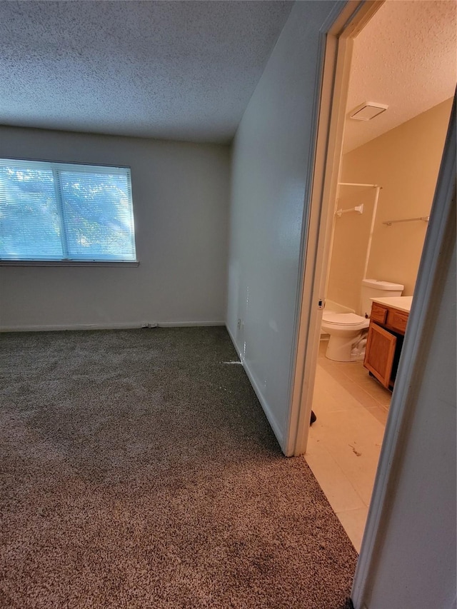 unfurnished bedroom featuring light carpet, baseboards, ensuite bathroom, and a textured ceiling