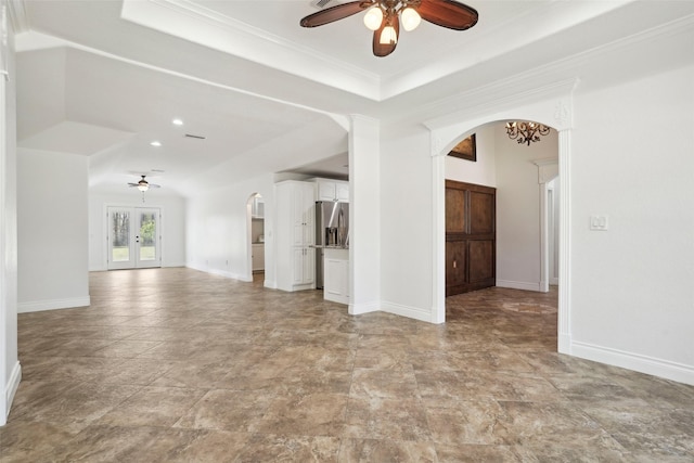 unfurnished living room featuring a tray ceiling, ceiling fan, arched walkways, and baseboards