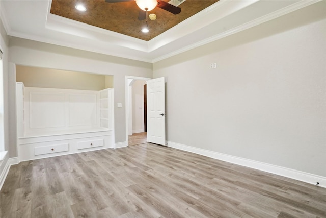 unfurnished bedroom featuring crown molding, a tray ceiling, baseboards, and light wood finished floors