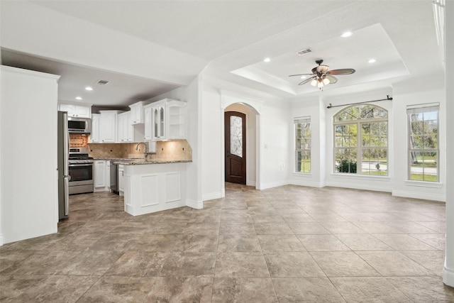 unfurnished living room with visible vents, a ceiling fan, arched walkways, and a raised ceiling