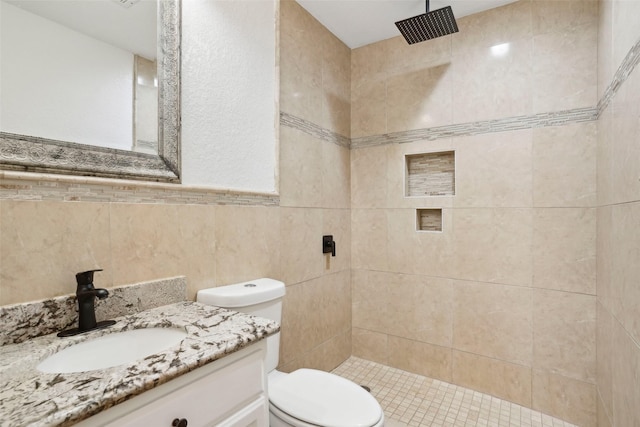 bathroom with a tile shower, tile walls, vanity, and toilet