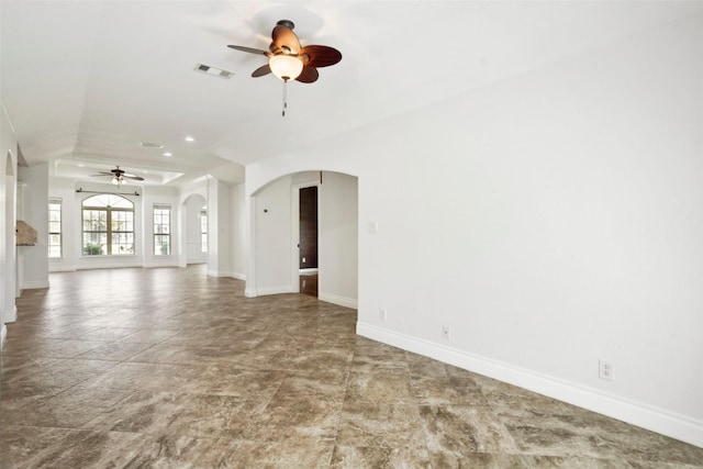 unfurnished living room with visible vents, baseboards, a ceiling fan, and arched walkways