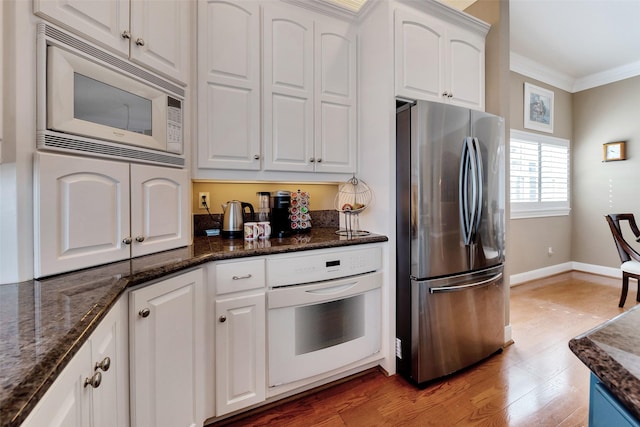 1306 Outrigger, Tiki Island, TX 77554 - kitchen with white appliances, crown molding, white cabinetry, light wood-type flooring, and dark stone counters