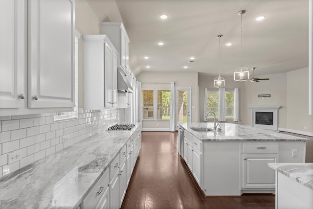 kitchen featuring white cabinets, a kitchen island with sink, a sink, open floor plan, and decorative backsplash
