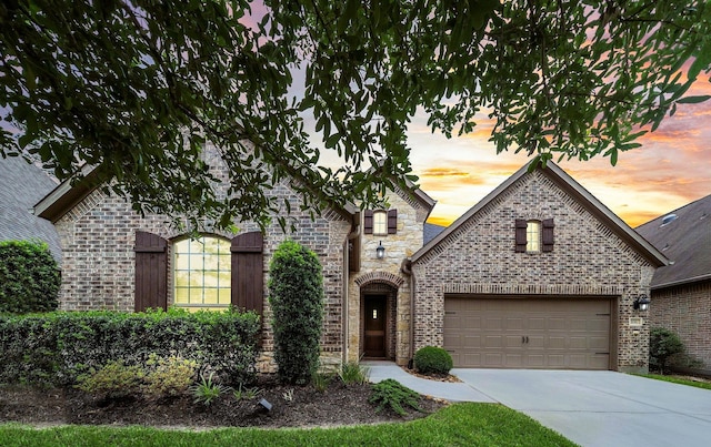 french country style house with driveway, a garage, and brick siding