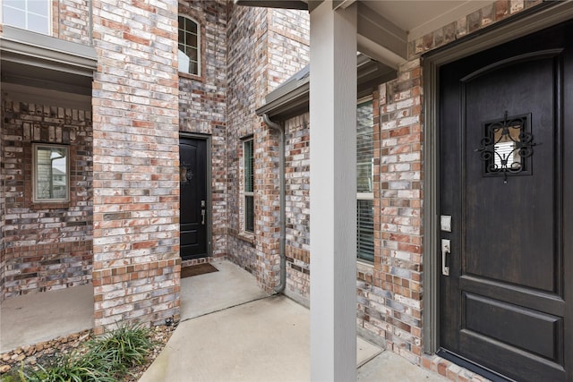 doorway to property featuring a porch and brick siding