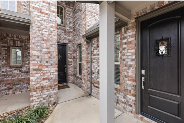 view of exterior entry with a porch and brick siding