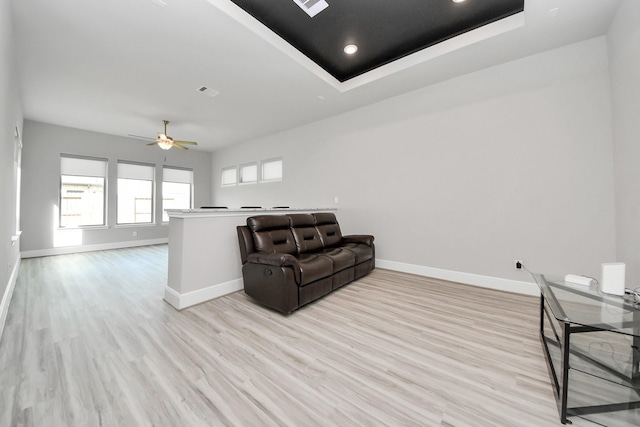 living area with baseboards, ceiling fan, light wood-style floors, and a raised ceiling