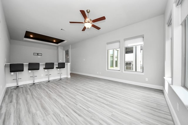 unfurnished living room with baseboards, wood finished floors, bar area, a ceiling fan, and a tray ceiling