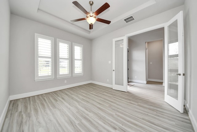 spare room featuring french doors, baseboards, a raised ceiling, light wood-style floors, and visible vents