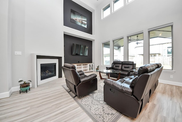 living area with baseboards, a high ceiling, wood finished floors, and a glass covered fireplace