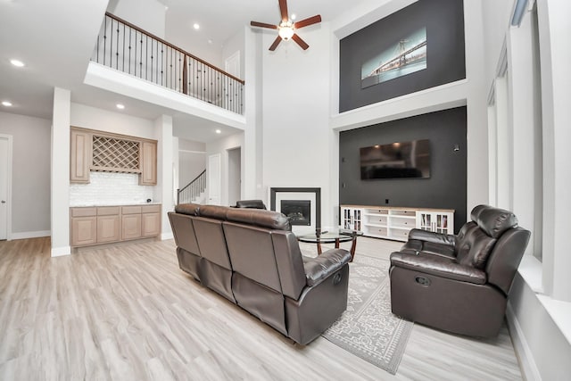 living room featuring stairs, a glass covered fireplace, light wood-type flooring, ceiling fan, and recessed lighting