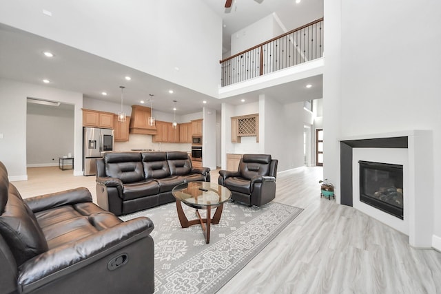living room with a ceiling fan, a glass covered fireplace, baseboards, light wood-style floors, and recessed lighting