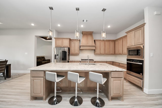 kitchen featuring light brown cabinetry, an island with sink, premium range hood, and appliances with stainless steel finishes