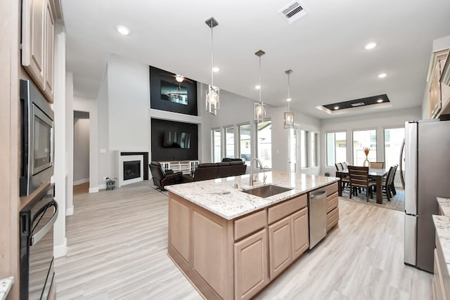 10015 Crescent Wood Dr, Missouri City, TX 77459 - kitchen with visible vents, a fireplace, stainless steel appliances, light brown cabinets, and a sink