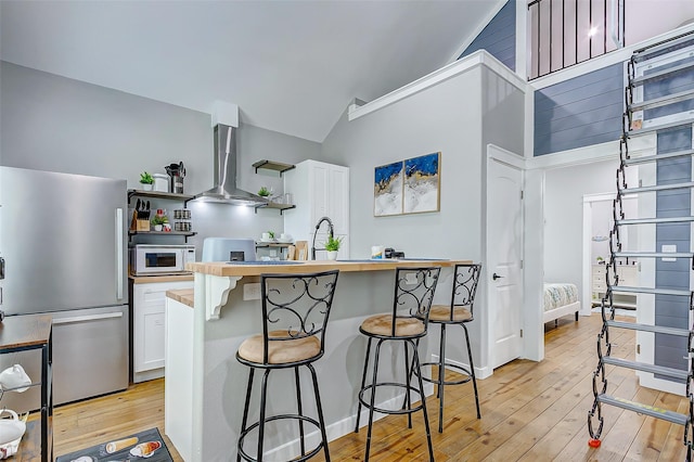 1079 Johnson Rd, Gilchrist, TX 77617 - kitchen with freestanding refrigerator, wall chimney exhaust hood, white microwave, light wood-style floors, and a breakfast bar area