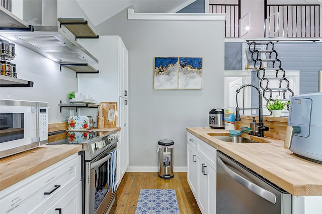 1079 Johnson Rd, Gilchrist, TX 77617 - kitchen featuring butcher block counters, stainless steel appliances, light wood-style flooring, wall chimney range hood, and open shelves