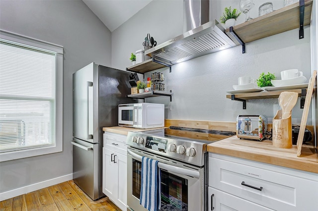 1079 Johnson Rd, Gilchrist, TX 77617 - kitchen featuring open shelves, stainless steel appliances, wall chimney exhaust hood, butcher block counters, and light wood-type flooring