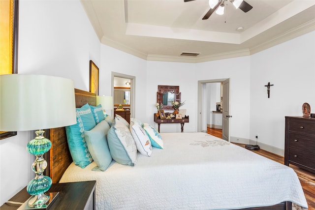 bedroom with visible vents, a tray ceiling, wood finished floors, and crown molding