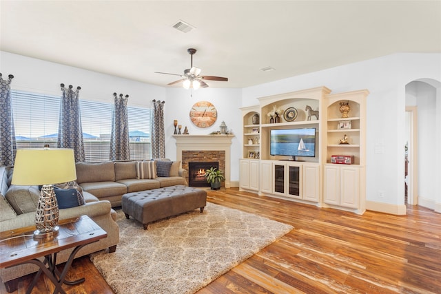 living area featuring light wood-type flooring, arched walkways, ceiling fan, visible vents, and a stone fireplace