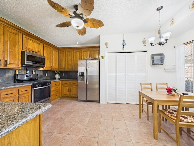 13523 Pasa Robles Ln, Houston, TX 77083 - kitchen featuring backsplash, brown cabinetry, light tile patterned floors, ceiling fan with notable chandelier, and stainless steel appliances