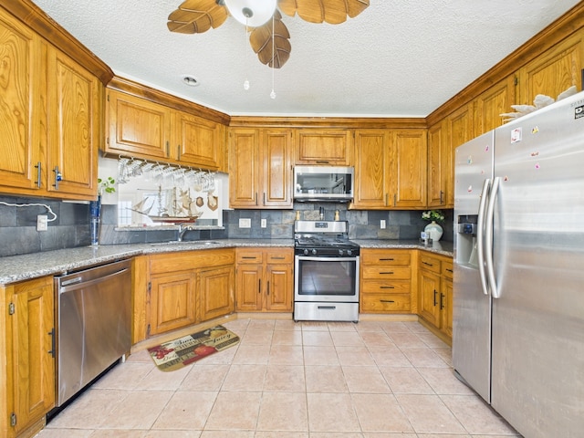 13523 Pasa Robles Ln, Houston, TX 77083 - kitchen with brown cabinets, a ceiling fan, appliances with stainless steel finishes, a sink, and light tile patterned floors