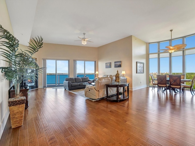 living area with a ceiling fan, a fireplace, a high ceiling, wood finished floors, and baseboards