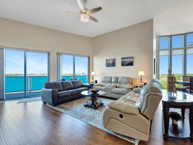 living area with a wealth of natural light, a water view, ceiling fan, and wood finished floors