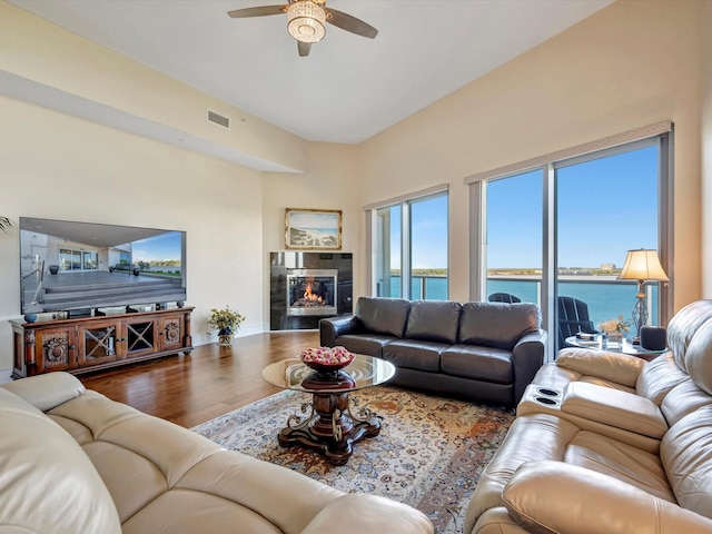 living room with visible vents, a high end fireplace, baseboards, wood finished floors, and a ceiling fan