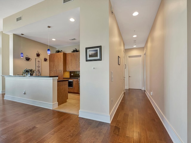 corridor featuring baseboards, visible vents, wood finished floors, and recessed lighting