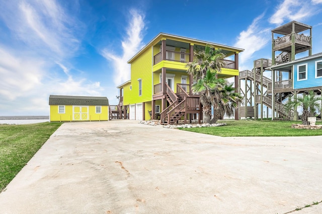 beach home with an outdoor structure, concrete driveway, stairway, a water view, and a storage shed