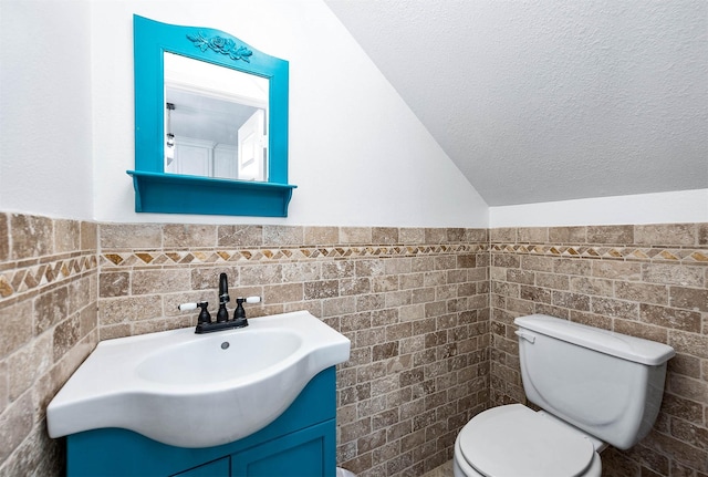 half bath with wainscoting, toilet, vanity, and a textured ceiling