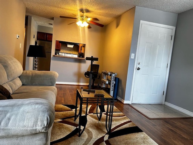 living room with baseboards, a textured ceiling, wood finished floors, and a ceiling fan